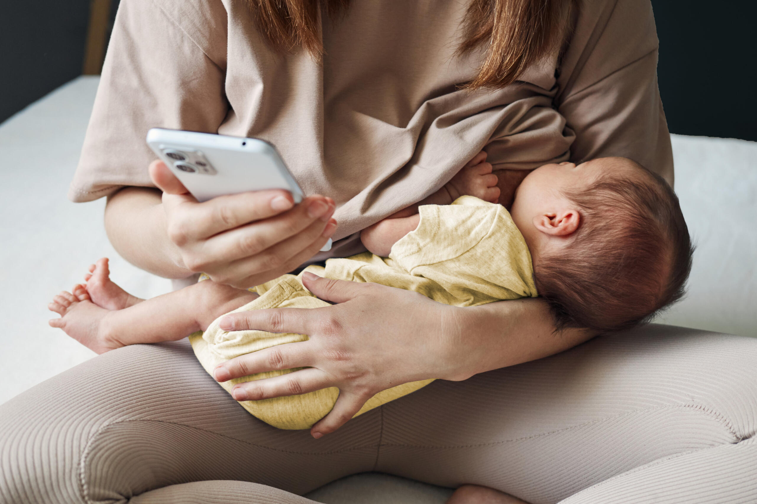 Mother breastfeeding her baby while she is using her cell phone